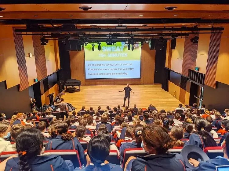 A full school auditorium during a Simple Six presentation on Sweat